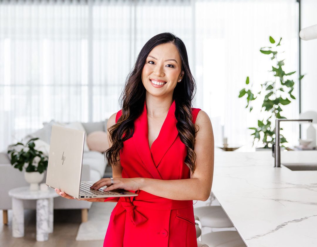 Charlyn in a red dress holding a laptop in a bright, modern kitchen